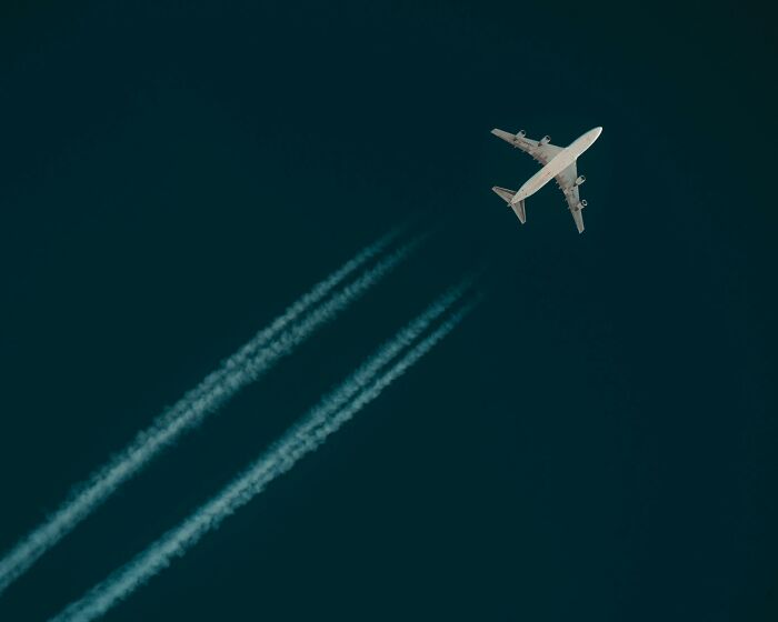 Airplane flying with contrails, evoking conspiracy theories about chemtrails in a clear sky.