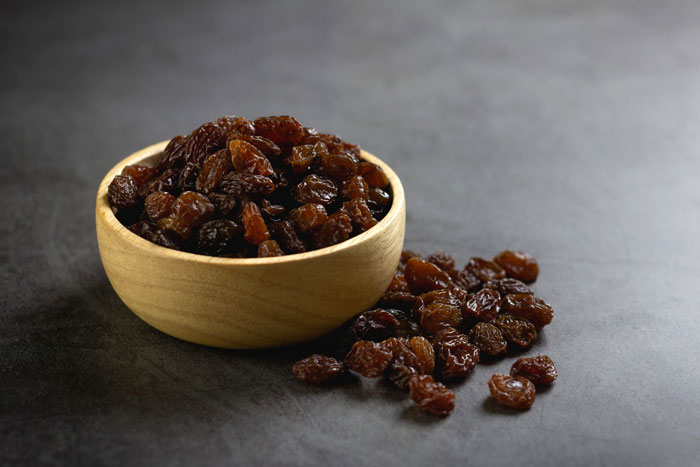 Wooden bowl filled with raisins, highlighting the debated ingredient in Costco's carrot cake recipe.