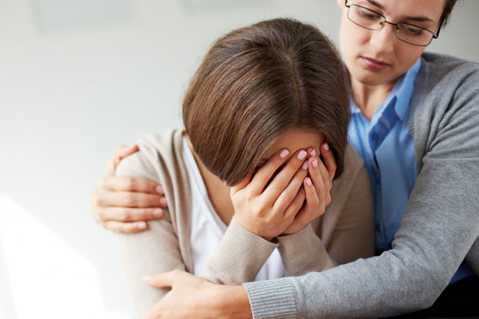 A woman comforted by a coworker, discussing a gluten-free diet and personal boundaries in a workplace setting.