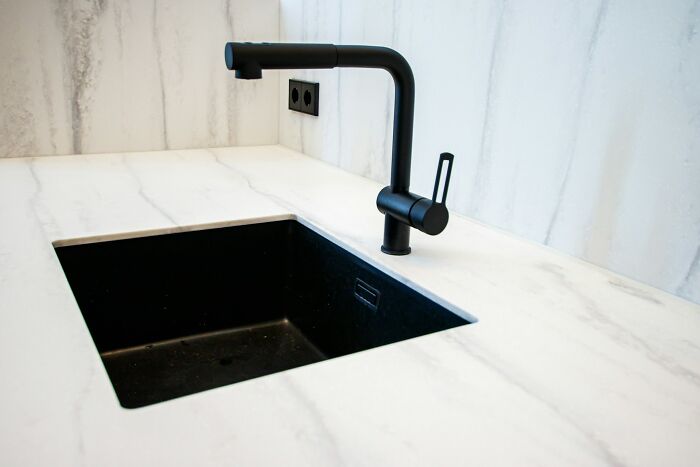 Modern kitchen with a sleek, minimalist black vessel sink and faucet on a white countertop.