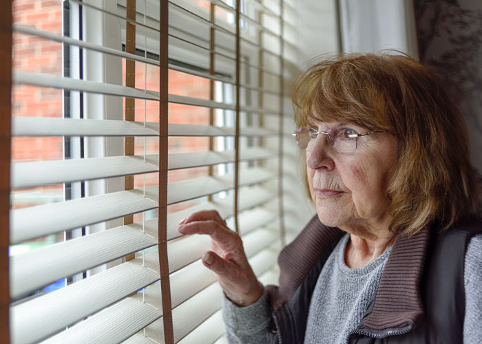 Elderly woman peering through blinds, representing crazy neighbor in a legal conflict scenario. Elderly woman peering through blinds, representing crazy neighbor in a legal conflict scenario.