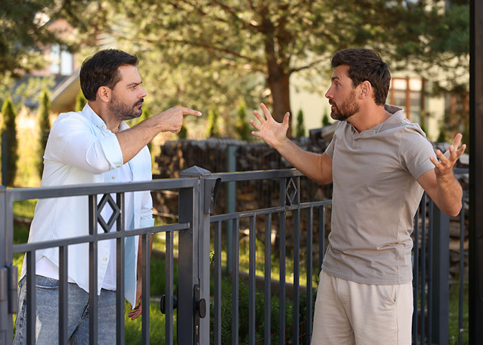 Two neighbors arguing over a fence in a heated dispute, showcasing neighborhood conflict and tension. Two neighbors arguing over a fence in a heated dispute, showcasing neighborhood conflict and tension.