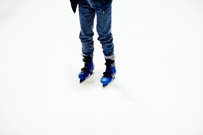 Person wearing blue ice skates on a rink, mid-motion, showcasing a playful April 1st vibe.