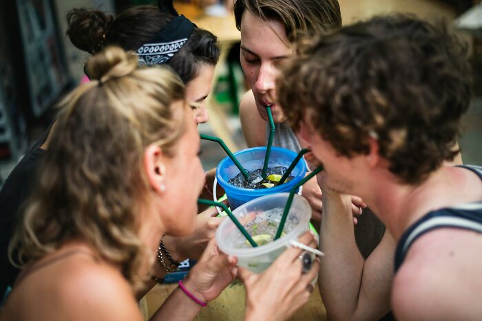 Group of young adults sharing drinks with straws outdoors, enjoying a super normal thing country social moment.