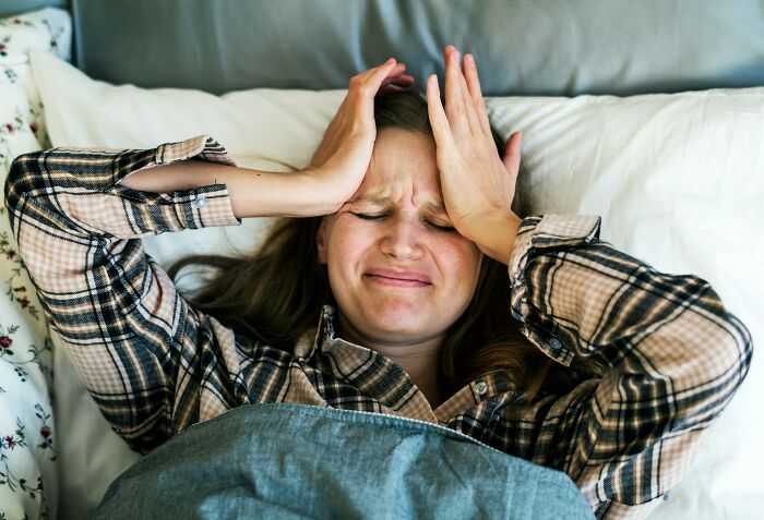 Woman in bed holding her head in frustration, illustrating unfair treatment from doctors causing distress.