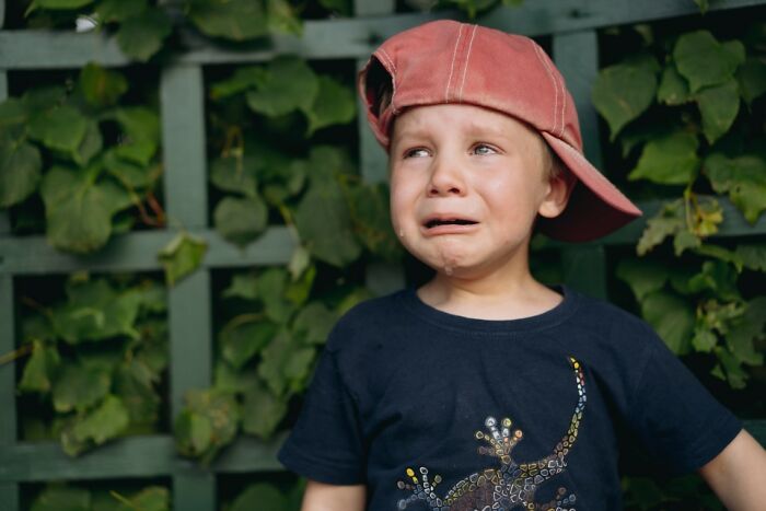 Child wearing a cap sideways, making a funny crying face.