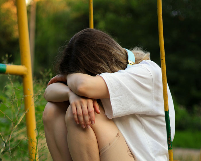 Teen girl sitting alone hugging knees on playground swing, reflecting family conflict over bi daughter lifestyle issues. Teen girl sitting alone hugging knees on playground swing, reflecting family conflict over bi daughter lifestyle issues.