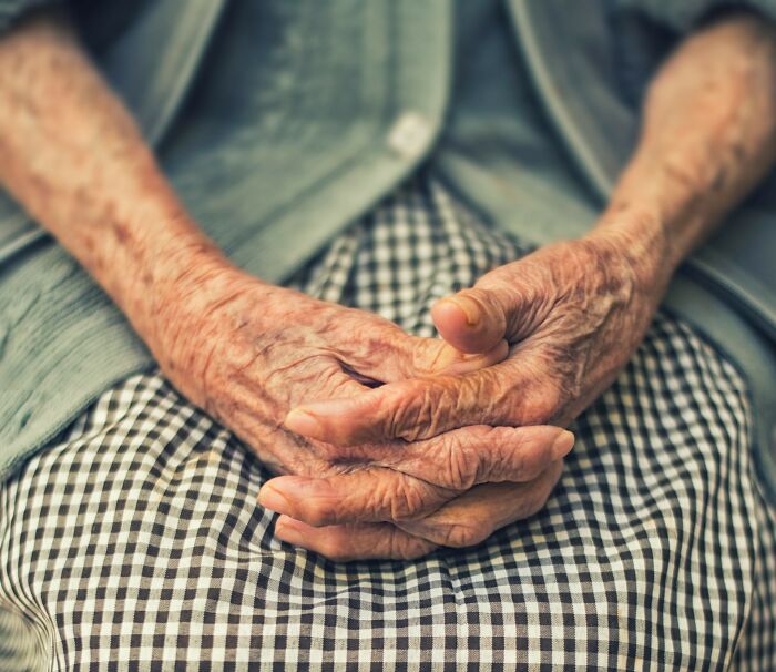 Elderly hands clasped over a checkered skirt, symbolizing a lifetime of experiences.