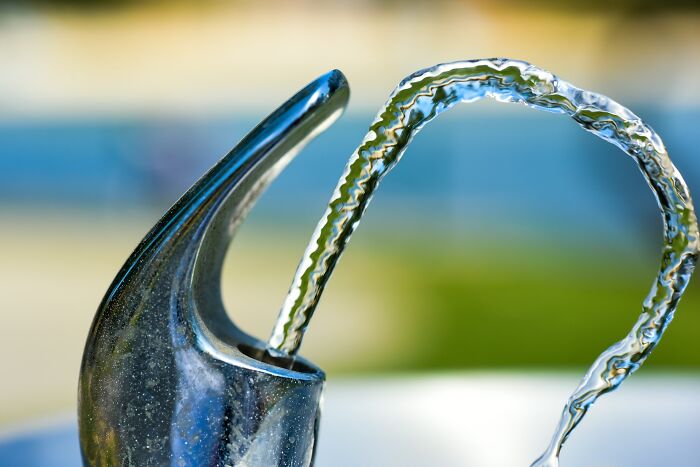 Close-up of a water fountain stream, highlighting the metallic nozzle with a clear background.