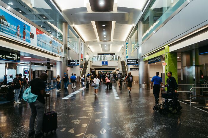 Passengers walking through a busy airport terminal, carrying luggage, highlighting adult tantrums in travel scenarios.