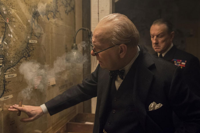 Actor portraying a historical figure, smoking a cigar while studying a map, showcasing dedication to difficult roles.