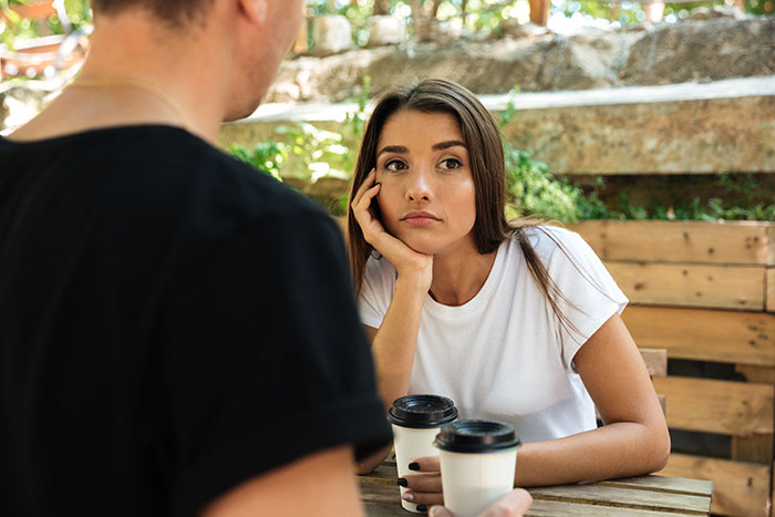Young woman looking thoughtfully at a man during a detailed discussion about dating perpetually single women outdoors.