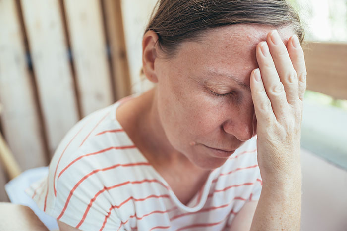 A woman in distress with hand on forehead, wearing a striped shirt, representing a tense family moment. A woman in distress with hand on forehead, wearing a striped shirt, representing a tense family moment.