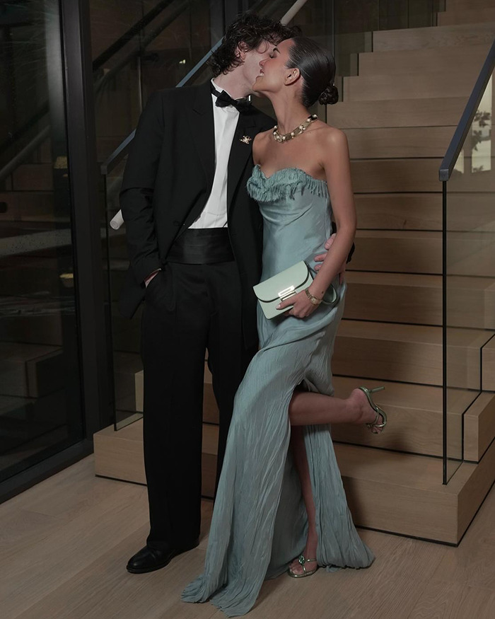 A couple elegantly dressed at an event, posing on a staircase, highlighting youthful celebration style.