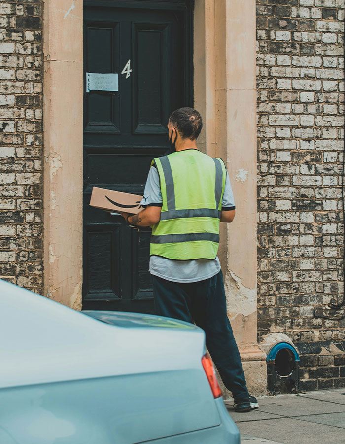 Delivery driver in a high-visibility vest stands at a door holding a package, ready to make a heroic impact.