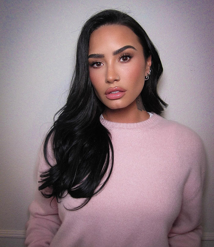 Person in a pink sweater with long dark hair, posing in a neutral setting.