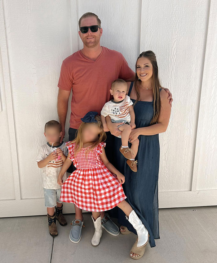 Family photo with parenting influencer and children, including 22-month-old son, standing against a white wall.