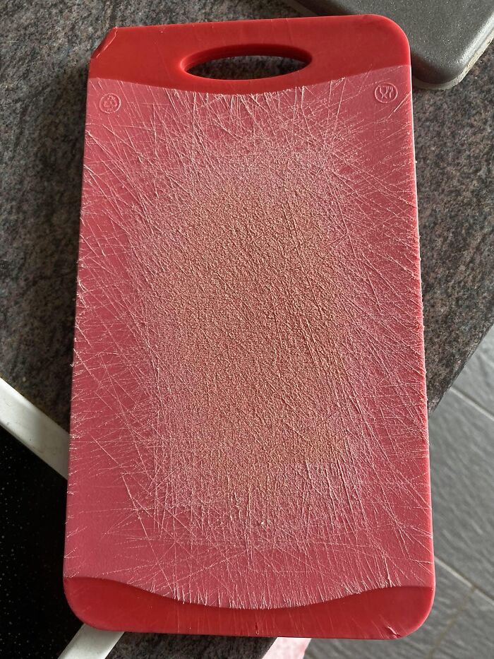 Heavily scratched red cutting board on a kitchen counter, highlighting potluck dish preparation challenges.