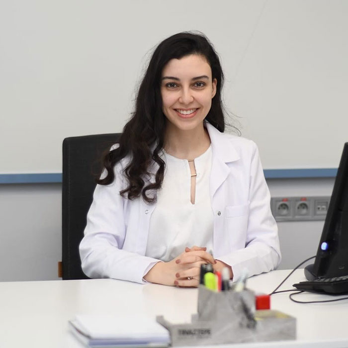 Smiling woman in a white coat sits at a desk, highlighting the impact of a botched nose job experience.