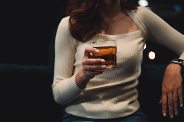 Woman holding a glass of aged scotch, casually seated, unaware of its $500 value.