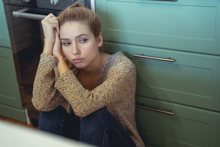 Woman sitting on kitchen floor, looking distressed after drinking aged scotch.