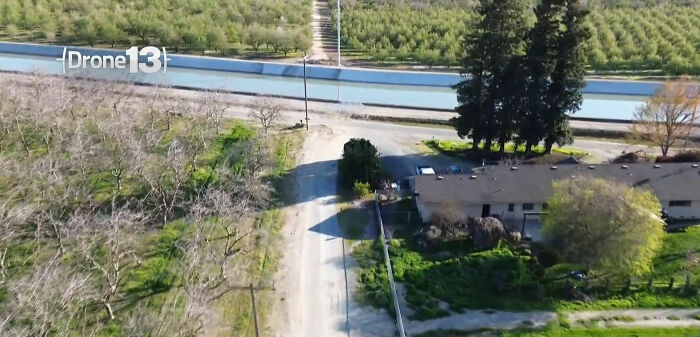 Aerial view of canal near a dirt road and trees; site of incident involving car crash.