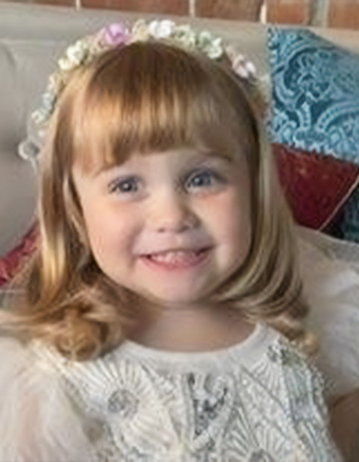 Young girl smiling, wearing a floral headband and white dress, representing a daughter involved in a canal incident.