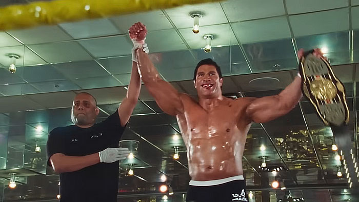 Dwayne Johnson showing his impressive transformation, shirtless and holding a wrestling championship belt in a celebratory pose.