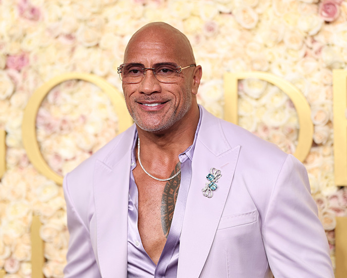Bald man in a lavender suit with glasses and a floral backdrop, sparking race confusion online.