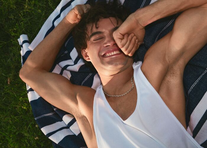 Man smiling and lying on a striped blanket outdoors, embracing freshness and good hygiene.