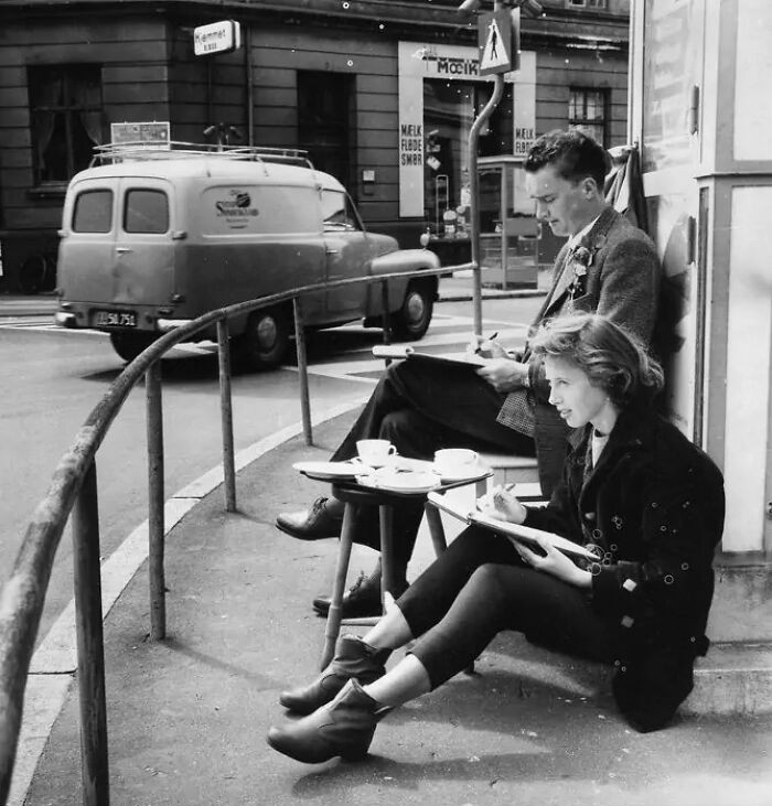 Young man and woman sketching outdoors at a street corner, capturing everyday life in Europe 100 years ago.