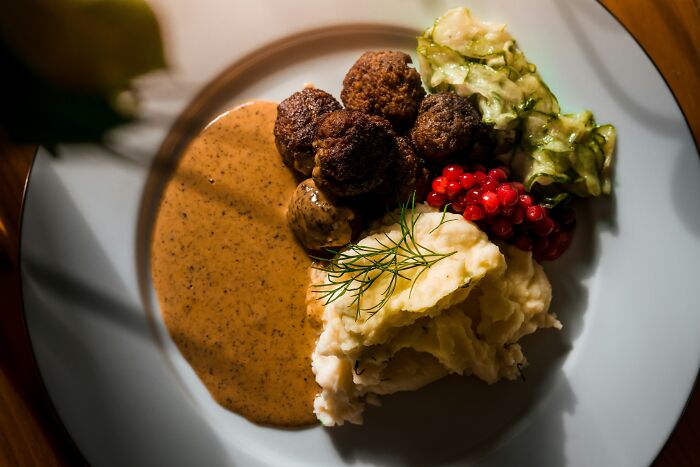 Plate with meatballs, mashed potatoes, gravy, lingonberries, and cucumber salad, showcasing a top dish from different countries.