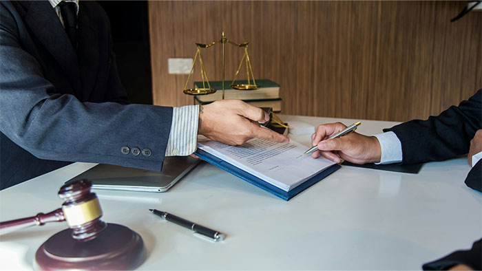 Two professionals in suits reviewing confidential documents at a desk with a gavel and scales.