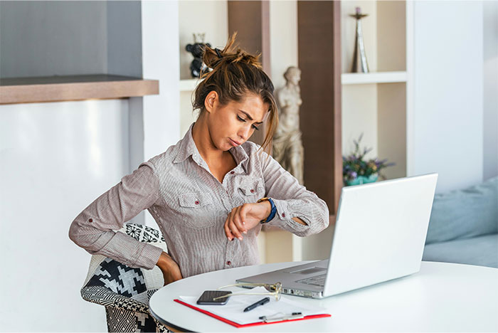 Woman at a desk checking her watch with a laptop open, symbolizing employee secrets in the workplace.