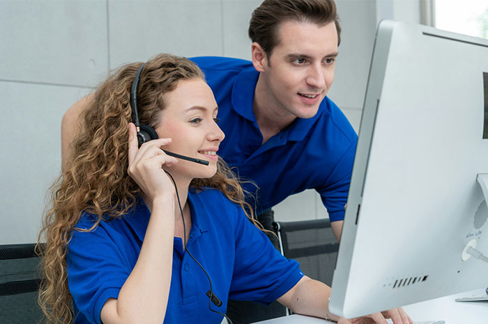 Two employees in blue shirts at a computer, maintaining focus and communication in a professional setting.