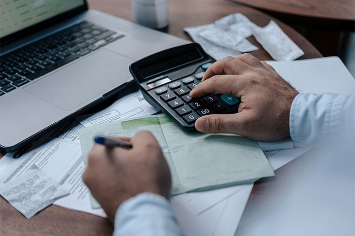 Person using a calculator at a desk, surrounded by receipts and a laptop, highlighting employee knowledge gaps.