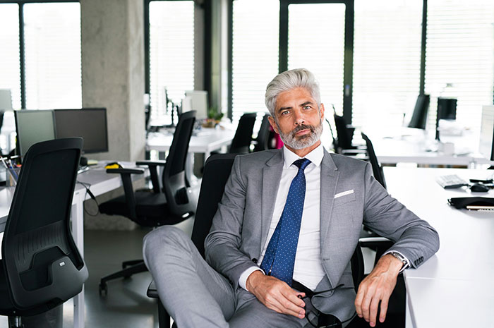Man in a gray suit sitting confidently in a modern office, depicting things employers don’t want their employees to know.