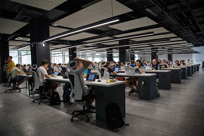 Employees working in a large open-plan office, seated at desks with computers.