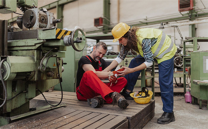 Worker in red overalls sitting, being aided by a colleague in a high-vis vest, highlighting common challenges employees face.