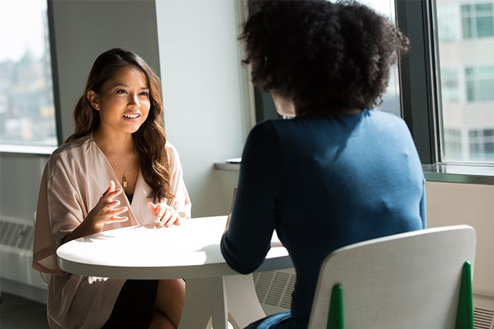 Two women having a discussion at a table, possibly about workplace secrets employees aren't aware of.
