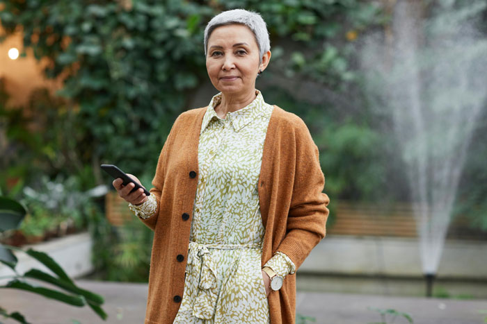 Middle-aged woman holding phone outdoors, symbolizing drama and secrets during bride’s wedding moments. Middle-aged woman holding phone outdoors, symbolizing drama and secrets during bride’s wedding moments.