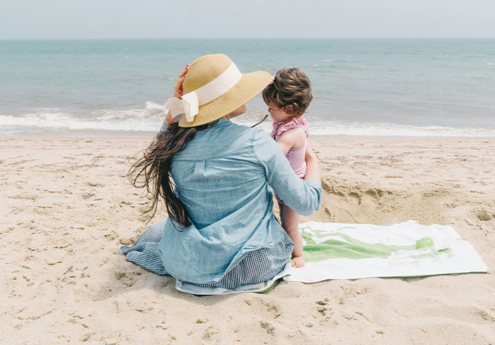 Woman sitting on the beach with a child, contemplating Easter vacation plans without her sister.