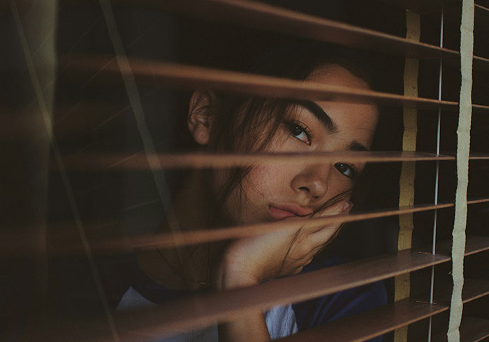 Woman thinking, looking through window blinds, contemplating Easter vacation decision.