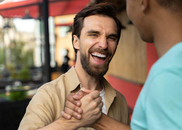 Man smiling and shaking hands outdoors, capturing a friendly moment that reveals American traits while traveling in Europe.