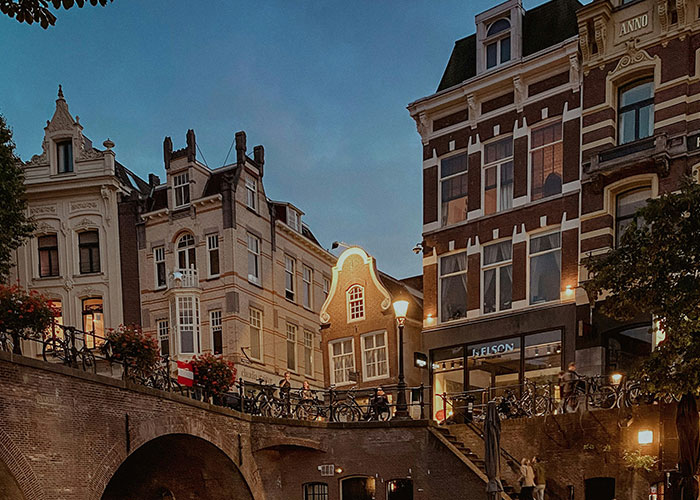 European street scene at dusk with historic buildings and canal bridge, highlighting architectural style.