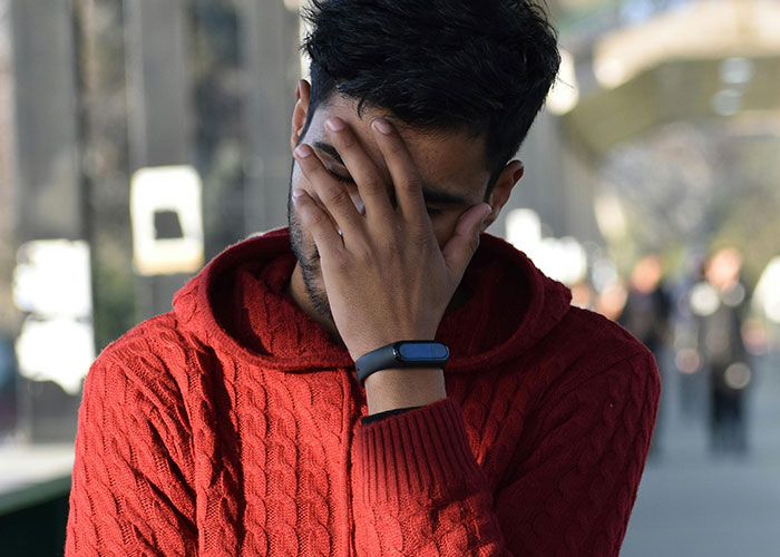 Person in a red sweater covering face with hand, conveying embarrassment; concept of Americans traveling in Europe.