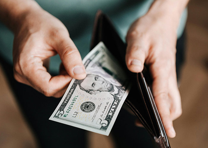 Hands holding a wallet with a visible five-dollar bill, symbolizing American travelers.