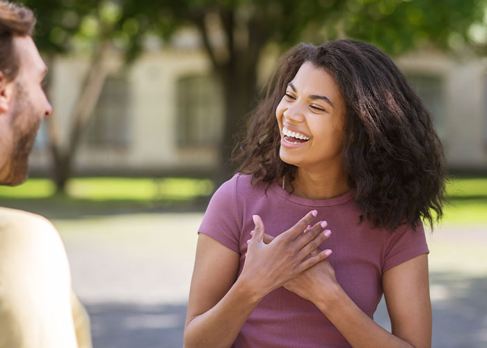 A woman laughing outdoors, talking, possibly revealing American traits while traveling.