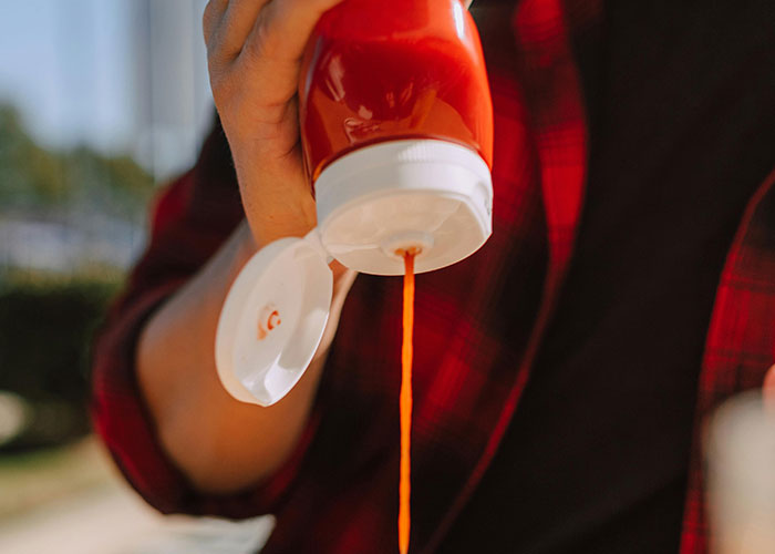 Person in red plaid pouring ketchup, highlighting American travel habits.
