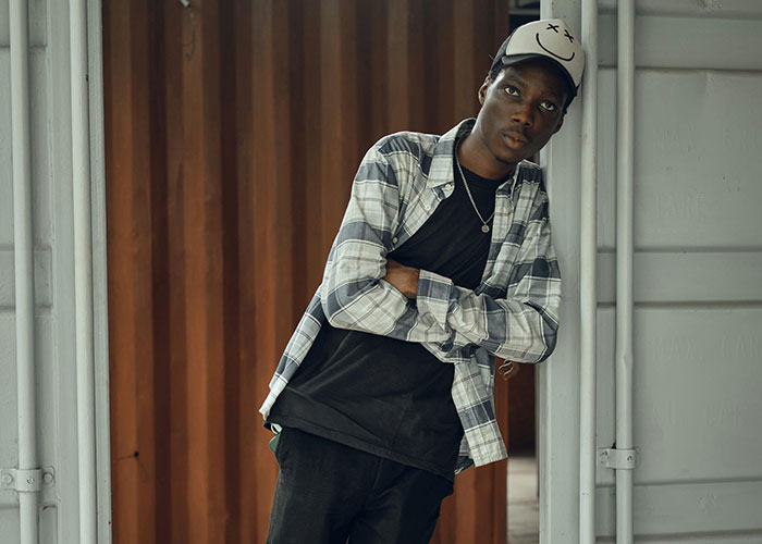 Man in casual attire leaning against a door, wearing a cap; captures American traveler style.